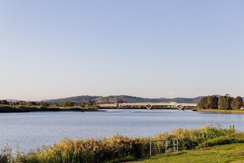 Een rivier met een brug, grasoevers en heuvels in de verte. 2