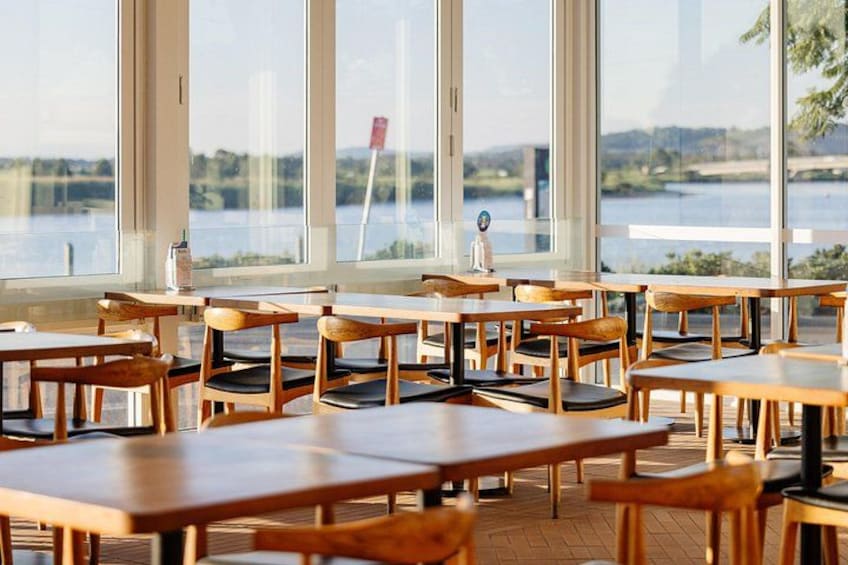 Een restaurant met houten tafels en stoelen, grote ramen en uitzicht op water. 2
