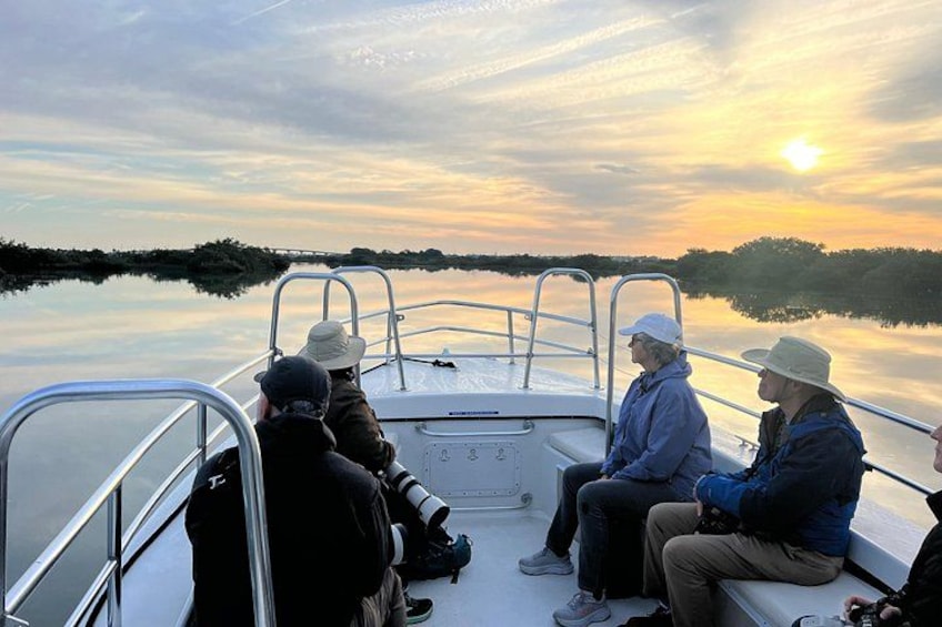 A group of people on a boat with a calm lake and a sunset in the background. 4