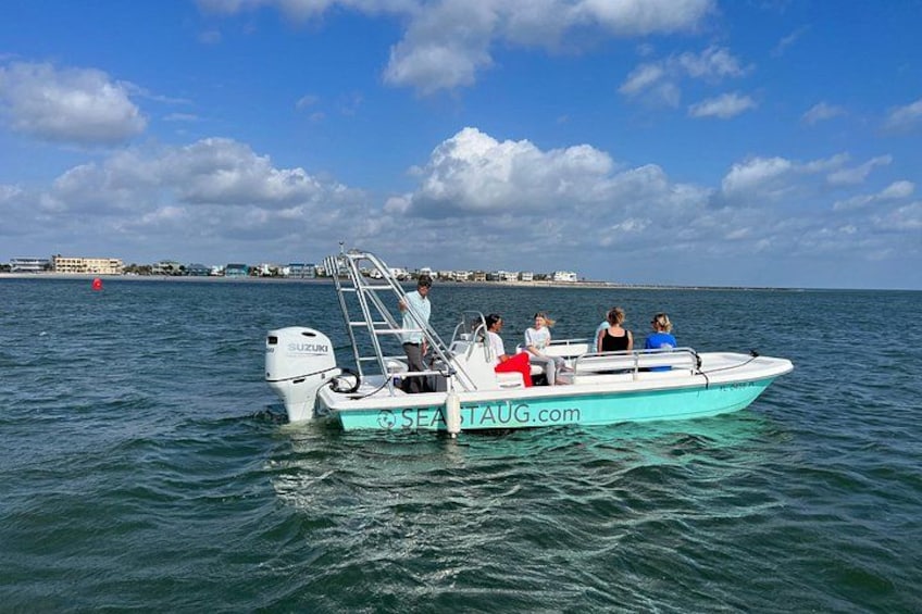 A small boat with people on it, floating on calm water with a clear sky and distant shoreline. 1