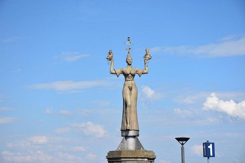 Una estatua de una mujer sosteniendo un báculo y una balanza, con un cielo azul despejado al fondo. 3
