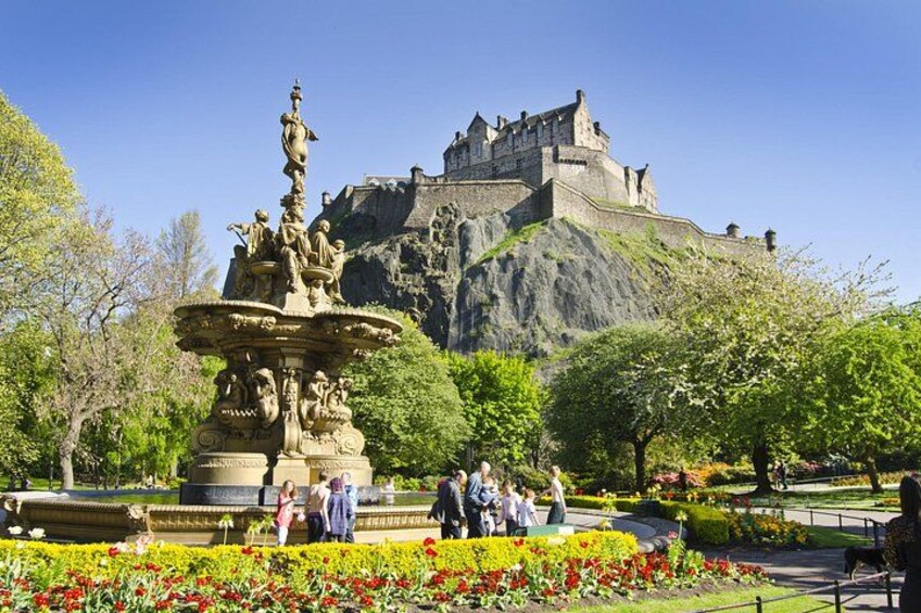 A castle on a hill, a fountain, and people in a park. 2