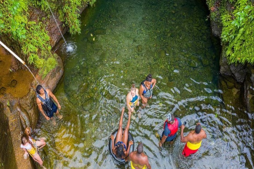 A group of people in a natural water setting, some standing and others in boats, surrounded by greenery. 3