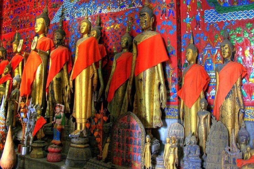 En samling gyldne Buddha-statuer pyntet med røde klæder foran en farverig, mønstret baggrund. 3