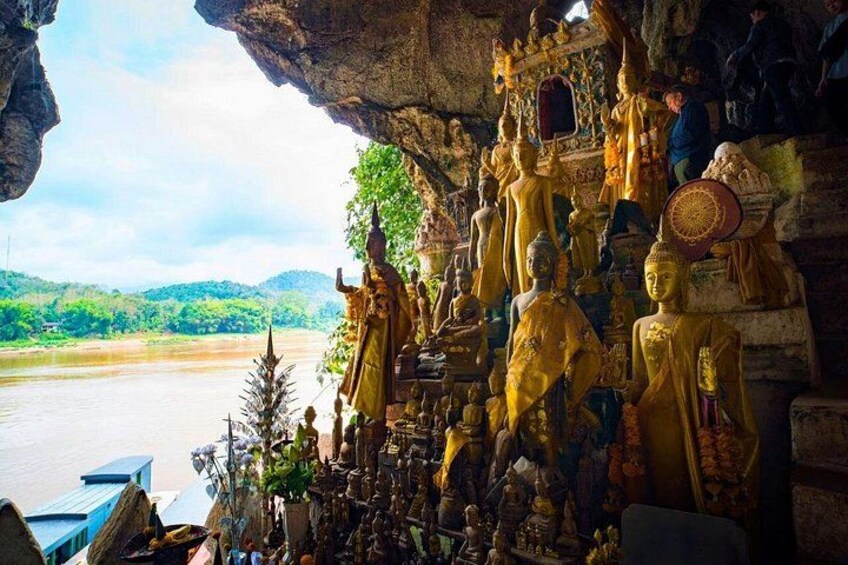 En grotta med gyllene Buddha-statyer och en flod i bakgrunden. 1