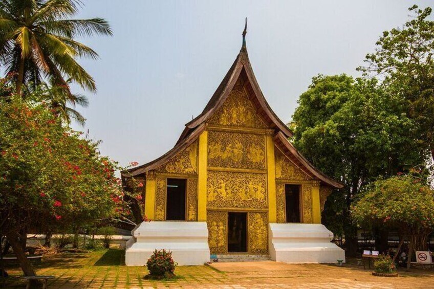 Et traditionelt tempel med detaljerede gyldne mønstre, omgivet af frodig vegetation og palmer. 2