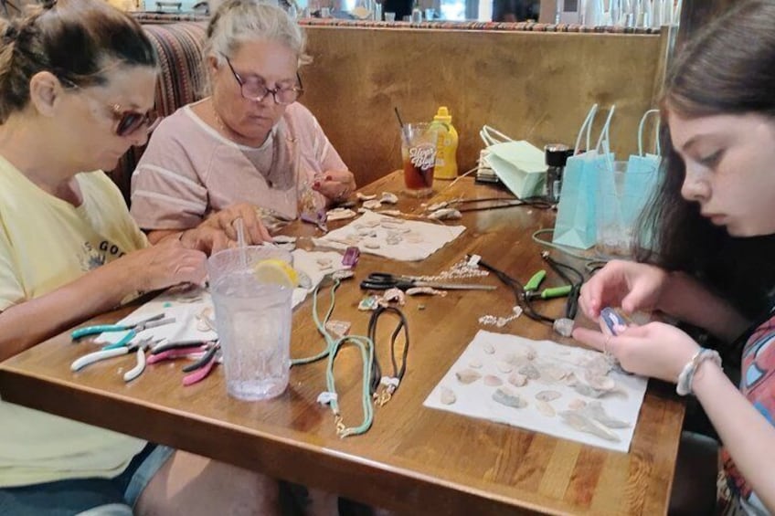 Three people engaged in a craft activity at a wooden table with crafting materials and tools. 3