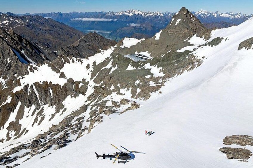A helicopter on a snow-covered mountain slope with rocky terrain and distant snow-capped peaks. 3