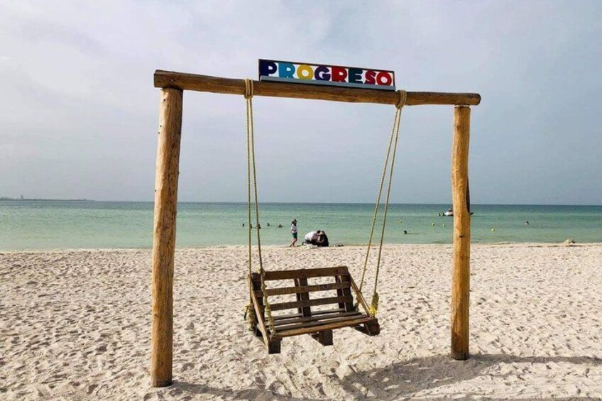 Une balançoire en bois, avec une pancarte indiquant « PROGRESO », sur une plage de sable, l’océan en toile de fond. 5