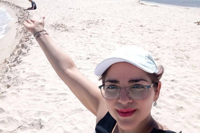 Une personne se tient sur une plage de sable, un bras levé, portant une casquette blanche et des lunettes. 2
