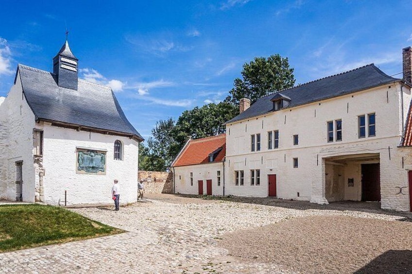 A cobblestone courtyard with white buildings, one with a black roof and a church steeple. 5