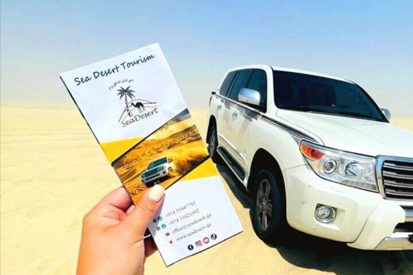A hand holding a brochure titled 'Sea Desert Tourism' with a white SUV parked on a sandy beach. 1