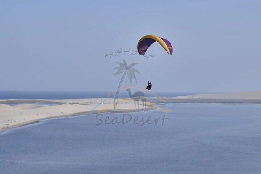 A person paragliding over a desert landscape with sand dunes and a clear sky. 2