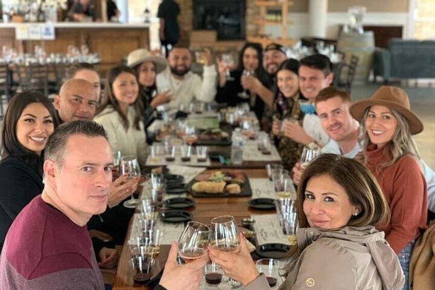 A group of people seated at a long table, holding wine glasses. 4