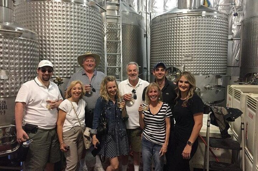 A group of people in a winery with stainless steel tanks and barrels. 2
