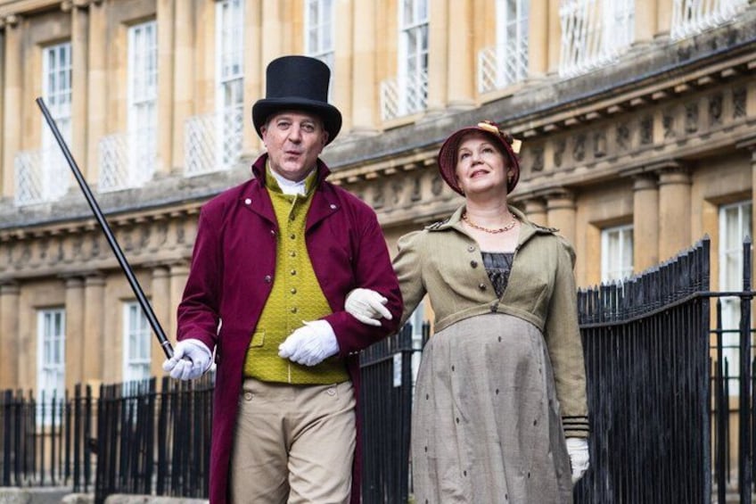 A man in a top hat and coat holding a cane, and a woman in a dress standing beside him. 2