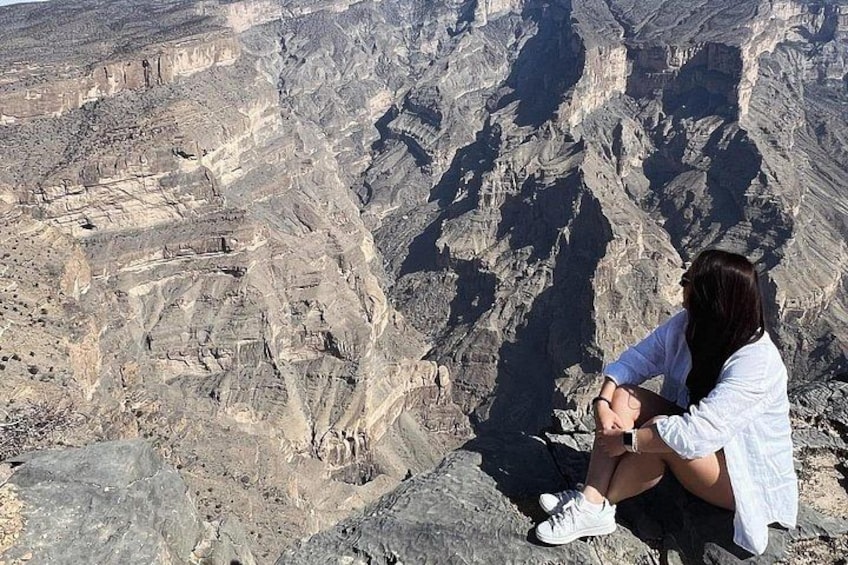 A person sitting on a rocky outcrop overlooking a canyon with layered rock formations. 4