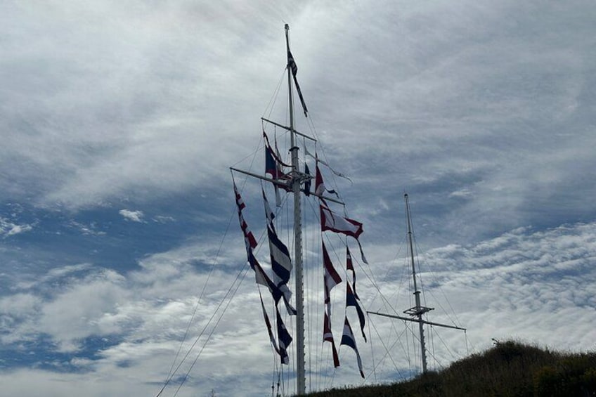 Un alto mástil con varias banderas, incluyendo una bandera roja y blanca destacada, contra un cielo parcialmente nublado. 2