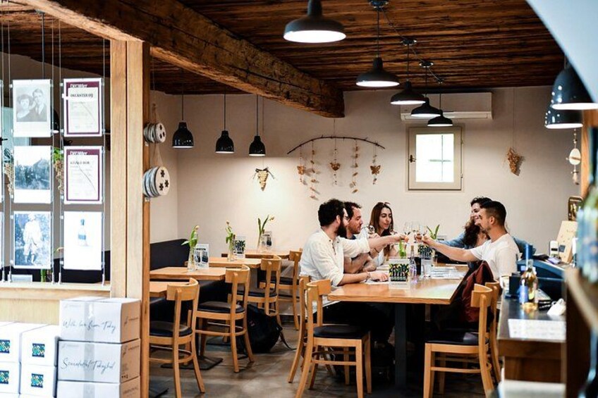 A group of people toasting at a wooden table in a rustic cafe with hanging lights and framed pictures on the wall. 1