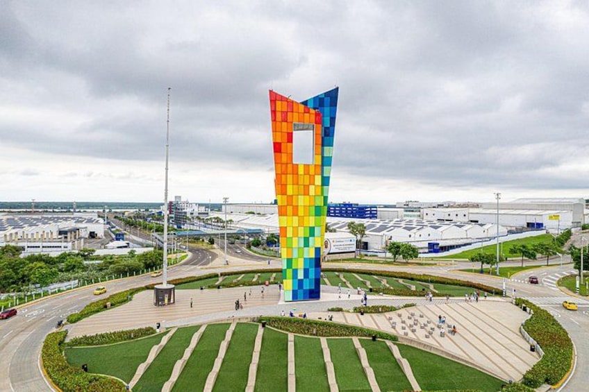 A tall, colorful tower with a checkered pattern, surrounded by a landscaped area with pathways and a roundabout. 1