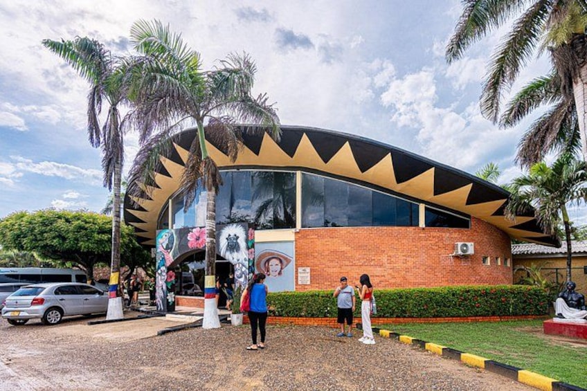 A modern building with a curved roof and large windows, surrounded by palm trees and a gravel path. 3