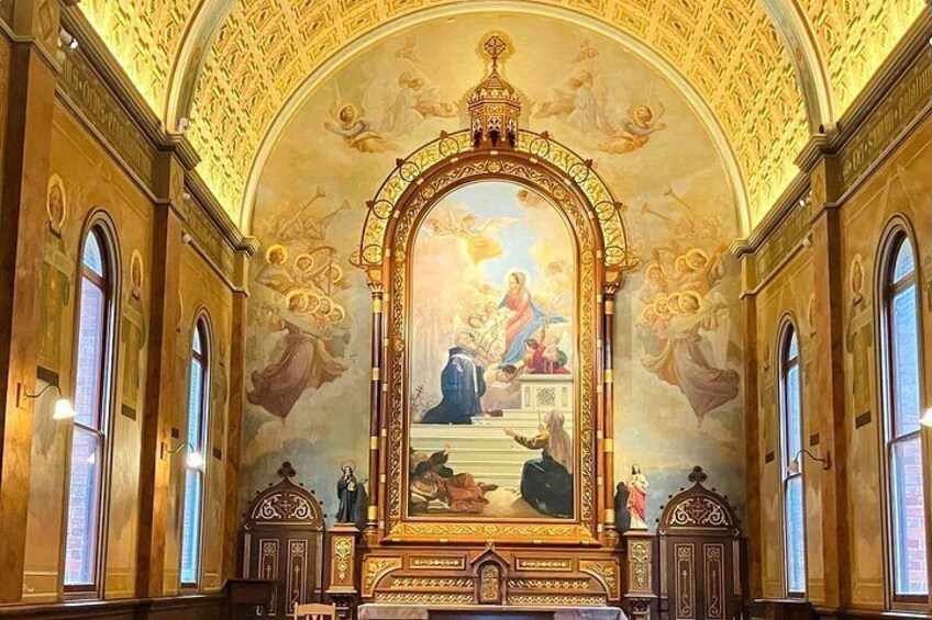 An ornate church interior with a large religious mural, arched windows, and detailed ceiling artwork. 1