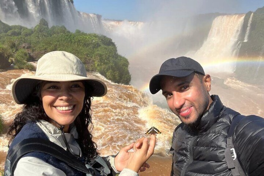 Deux personnes prenant un autoportrait devant une cascade, avec un arc-en-ciel en arrière-plan. 4