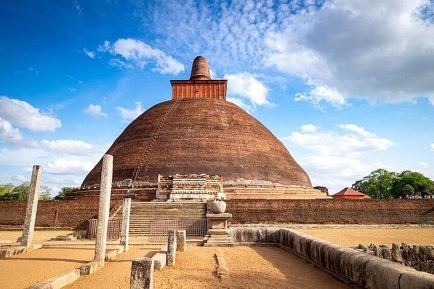 A large, domed structure with a stepped entrance, surrounded by a low wall and a sandy ground. 1