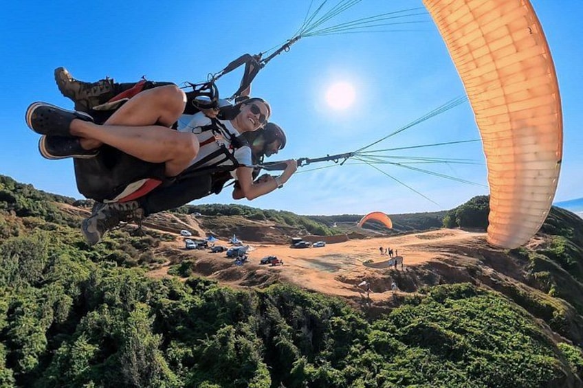 Une personne pratiquant le parapente avec un parachute, un ciel dégagé et un paysage vallonné à la végétation clairsemée. 1
