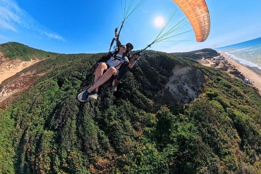 Une personne pratiquant le parapente au-dessus d’un paysage côtier, avec une végétation dense et une plage en arrière-plan. 5