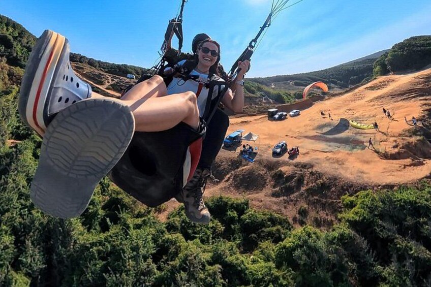 Une personne pratiquant le parapente avec un parachute, entourée d’un paysage vallonné et d’autres parapentistes. 3