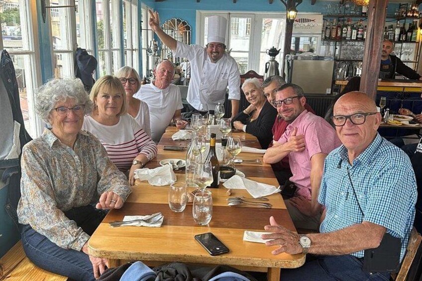 A group of people seated at a wooden table in a restaurant with bottles and glasses on it. 2