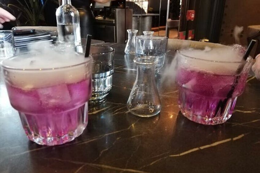Two glasses of a purple drink with ice cubes on a bar counter. 1