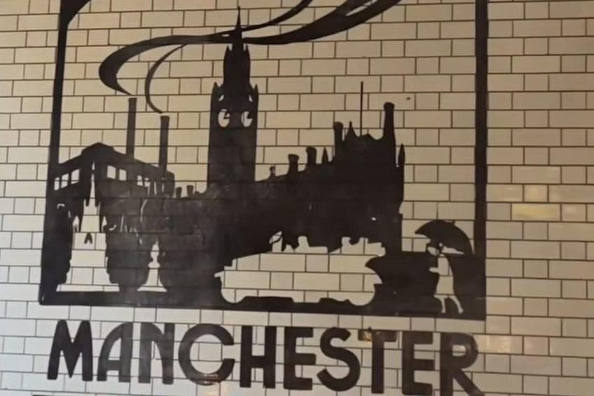 Una pared con una silueta negra de un paisaje urbano que incluye una torre del reloj, un puente y una estatua. Abajo de la silueta se lee la palabra 'MANCHESTER'. 3