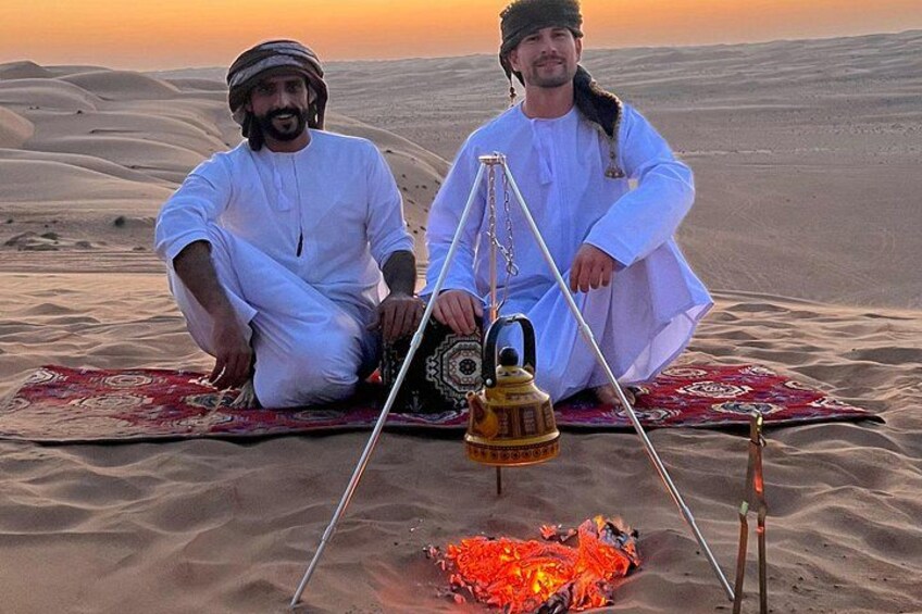 Two men sitting on a carpet in a desert with a fire and a traditional lamp. 3