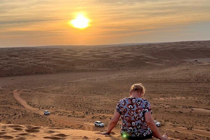 A person sitting on a dune with a desert landscape and a setting sun in the background. 5