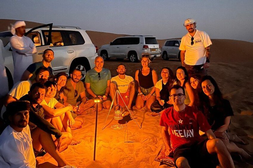 A group of people sitting around a campfire in a desert with vehicles in the background. 2