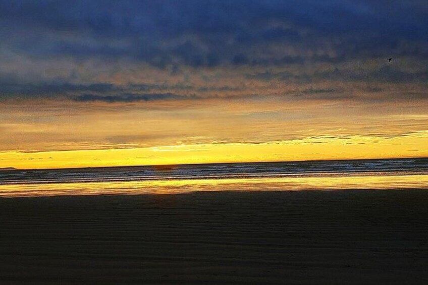 Un coucher de soleil sur une plage, avec un premier plan de sable sombre et un ciel nuageux. 2