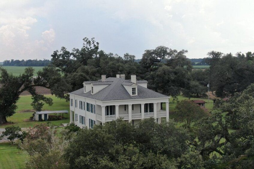 A large white house with a balcony, surrounded by lush greenery and trees. 3