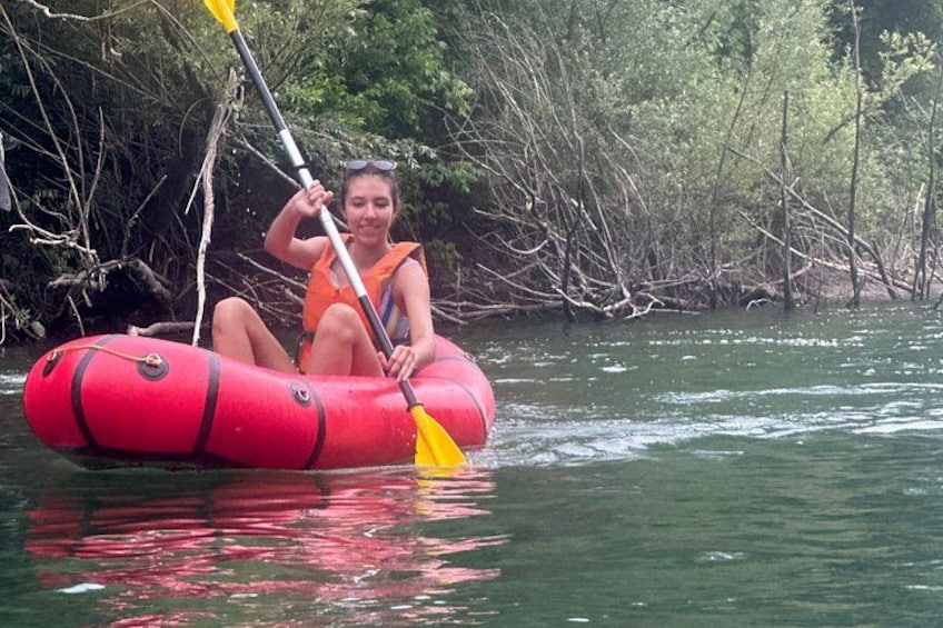 A person in a red inflatable raft on a river surrounded by dense vegetation. 5