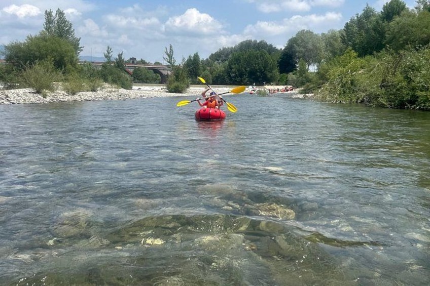 A person kayaking on a river surrounded by greenery and a bridge in the background. 2
