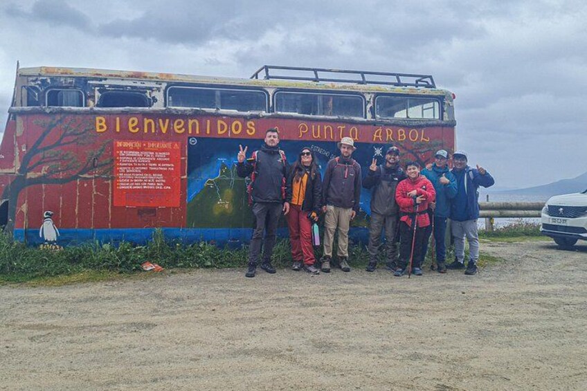 A group of people standing in front of a colorful bus with a mural, a sign, and a landscape in the background. 3