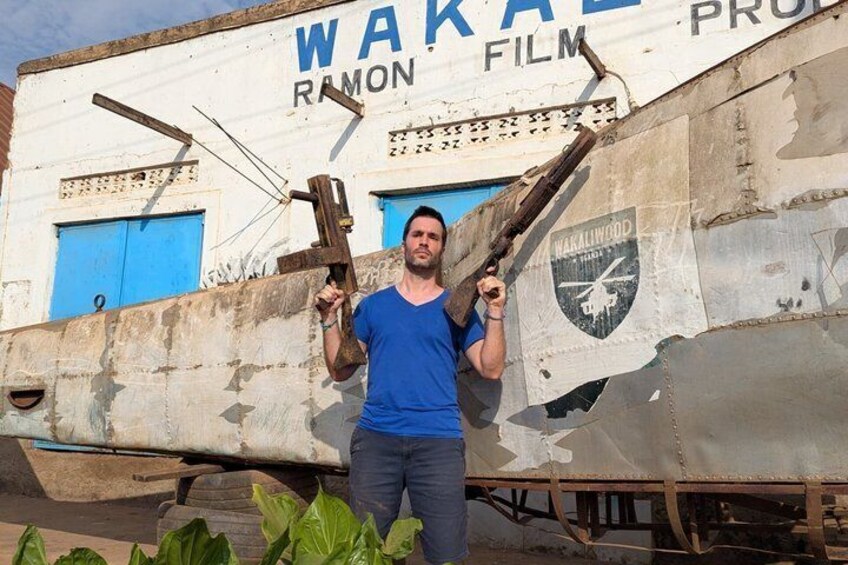 A man standing in front of a rusted aircraft with a ramonet film logo and a helicopter emblem. 4