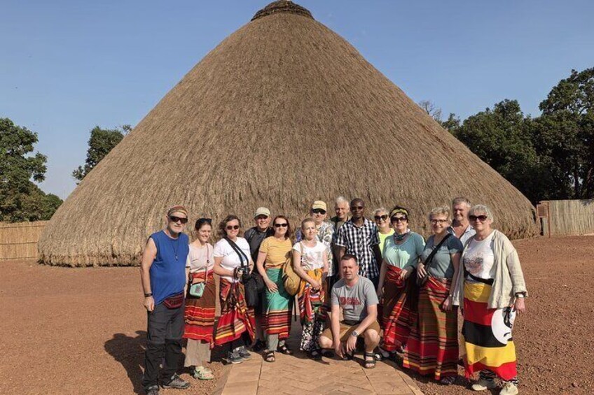 A group of people posing in front of a large thatched structure. 1