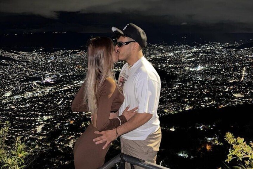 A couple kissing on a balcony overlooking a city at night. 5