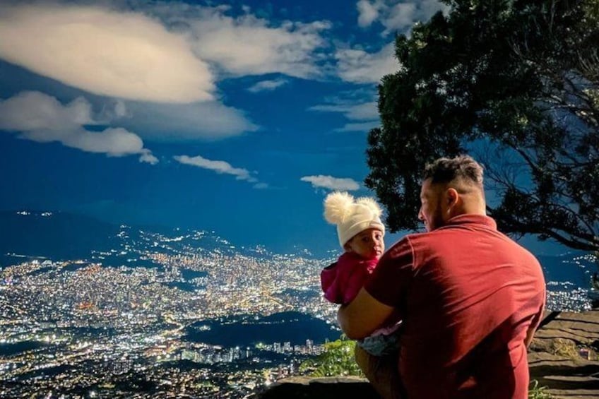 A person holding a child, overlooking a cityscape with buildings and a clear sky. 3