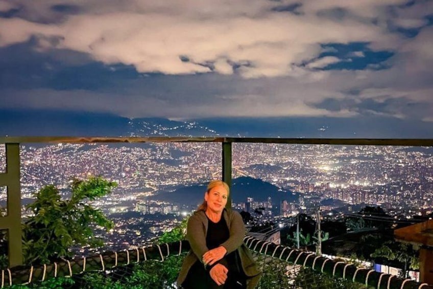 A person sitting on a balcony overlooking a cityscape at night. 2
