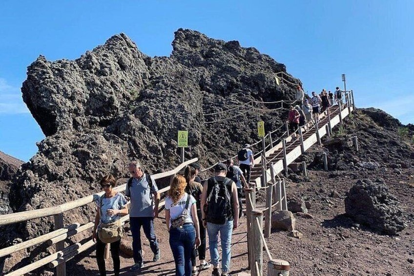 Un grupo de personas subiendo por una escalera de madera sobre terreno rocoso, con una gran formación rocosa al fondo. 3