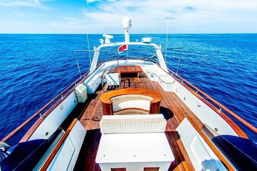 A boat deck with wooden flooring, white cushions, and a flag. 1