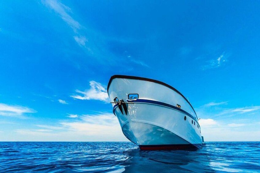 Ein Boot mit gebogener Bordwand, einer Kabine und einem roten Streifen, das auf ruhigem, blauem Wasser unter einem klaren Himmel treibt. 4